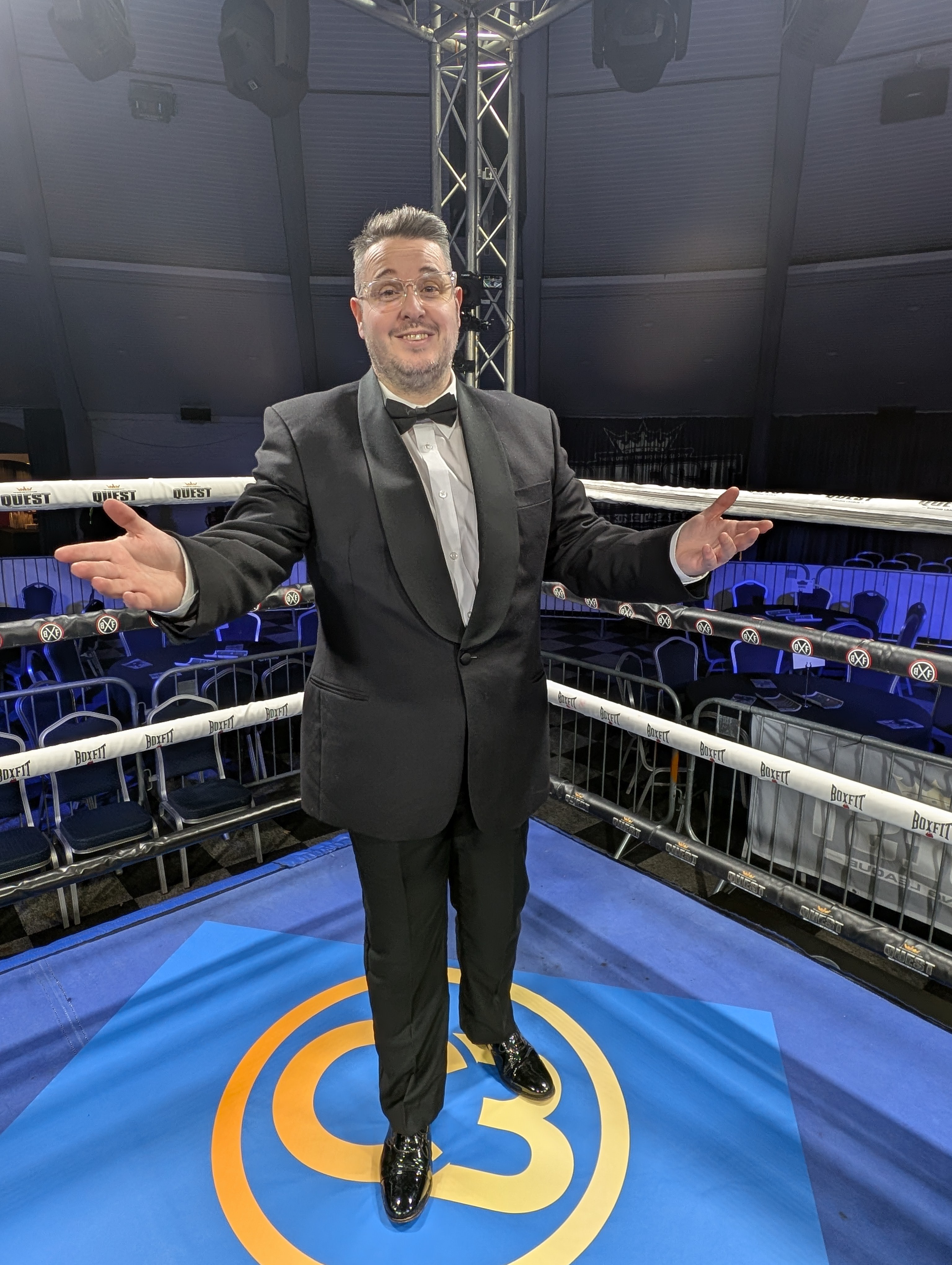 Jonathan Millard standing in a BoxFit boxing ring in formal tuxedo with arms wide open