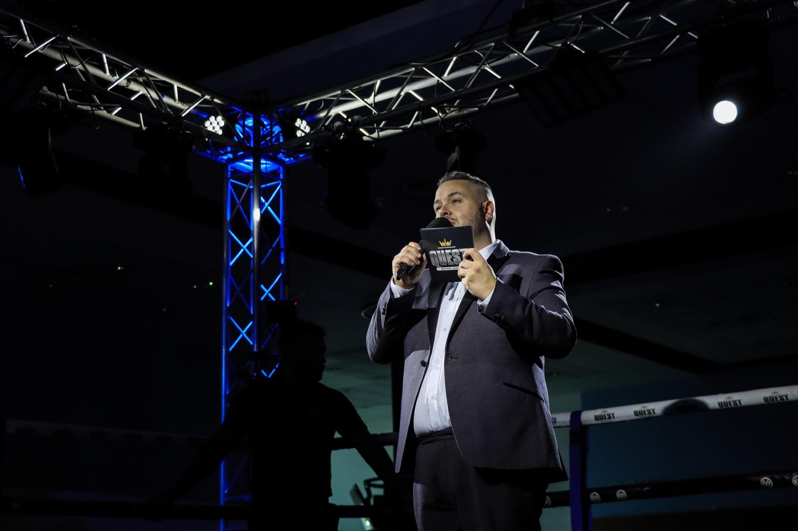 Jonathan Millard announcing at Quest Boxing event under blue stage lights