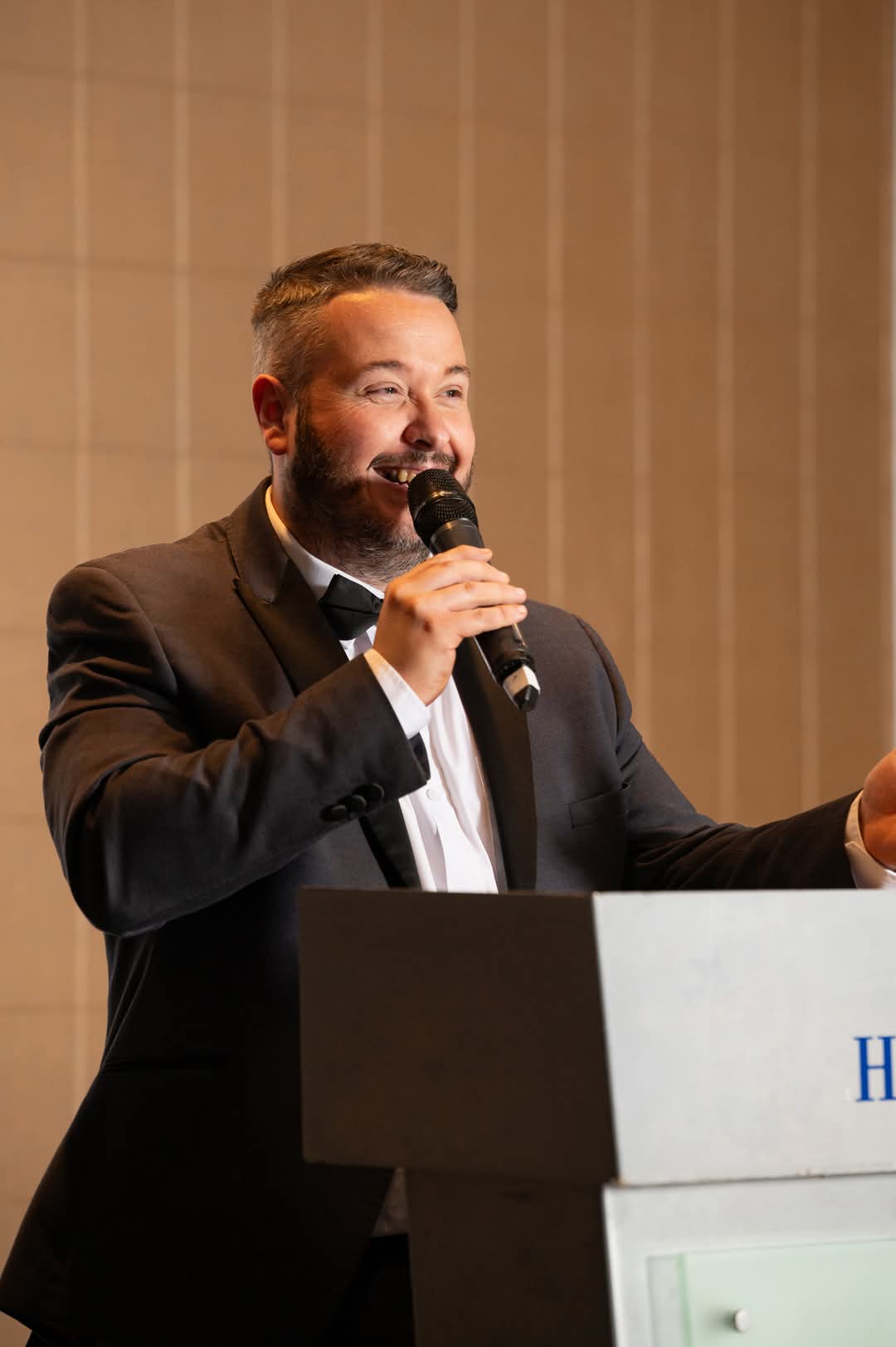 Jonathan Millard hosting a corporate gala at a podium in formal attire